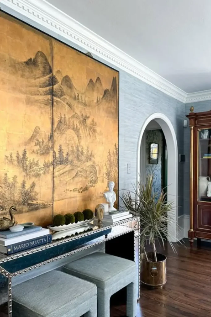 A studded console table decor with books, a small sculpture and Two upholstered ottomans slide neatly underneath.