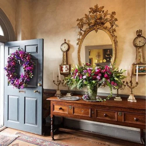 Gorgeous entryway table decor with a grand wooden, vintage console table crowned by an ornate gold mirror and a vibrant floral arrangement.