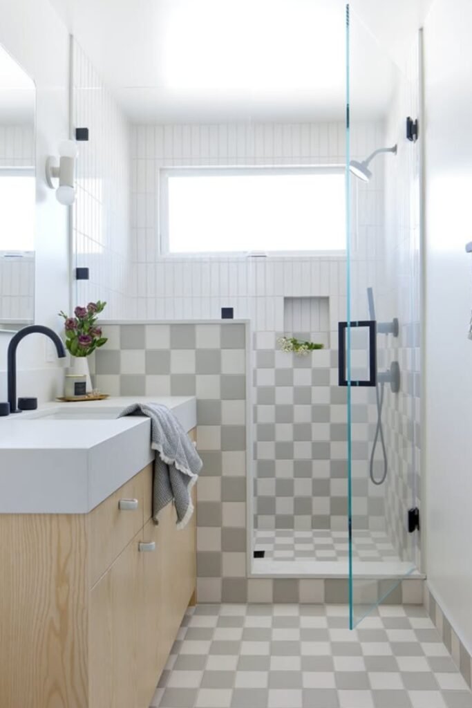 Scandinavian bathroom with pale grey and white checkered floor tiles and glass shower wall.