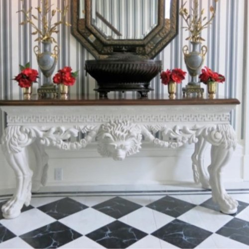 Ornate white console table and mirror with black and white checkered floor in a hallway.