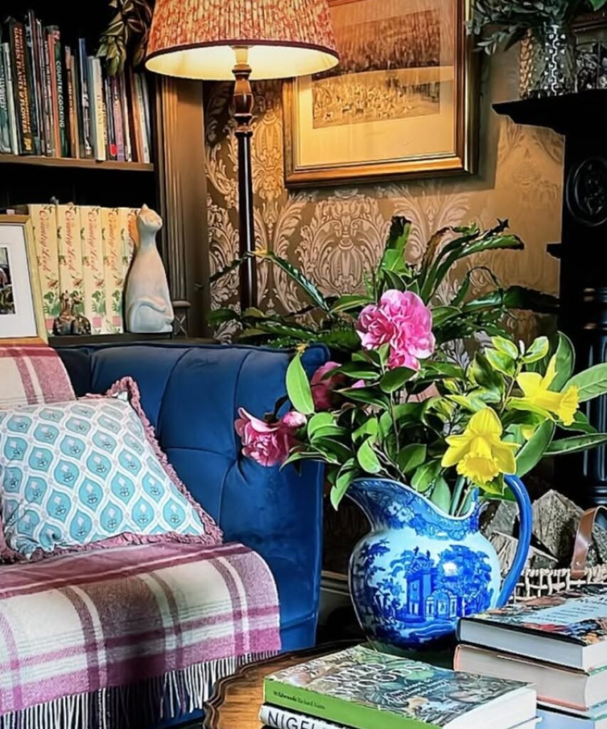 Blue pitcher used as vase with pink and yellow florals on a wooden table.