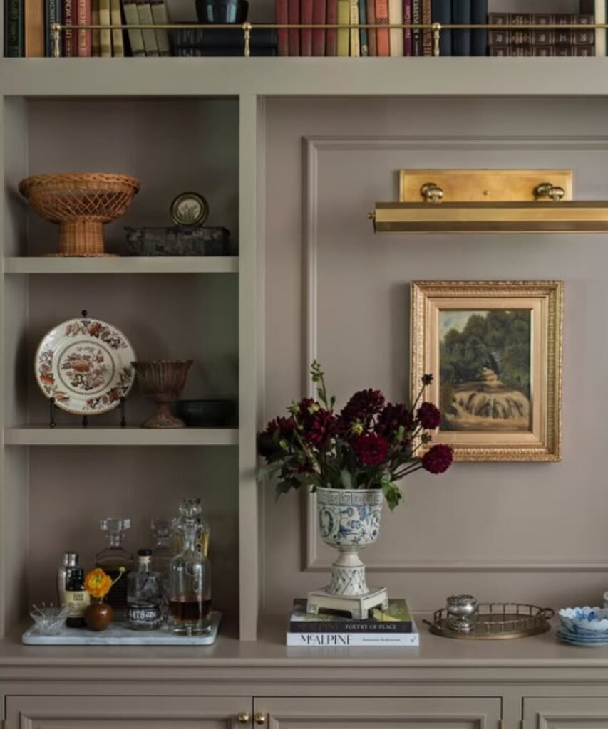 Decorative urn vase with deep red flowers on a beige console.
