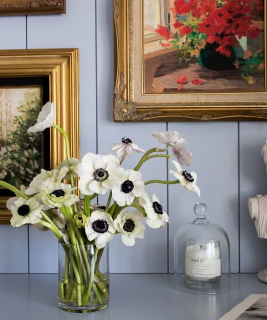 Glass vase with white anemone flowers in front of framed wall art.