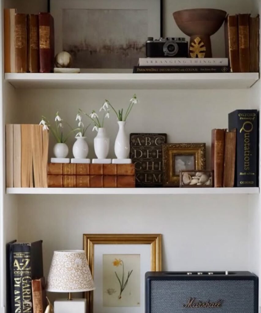 White bud vases with snowdrops arranged on a shelf with old books