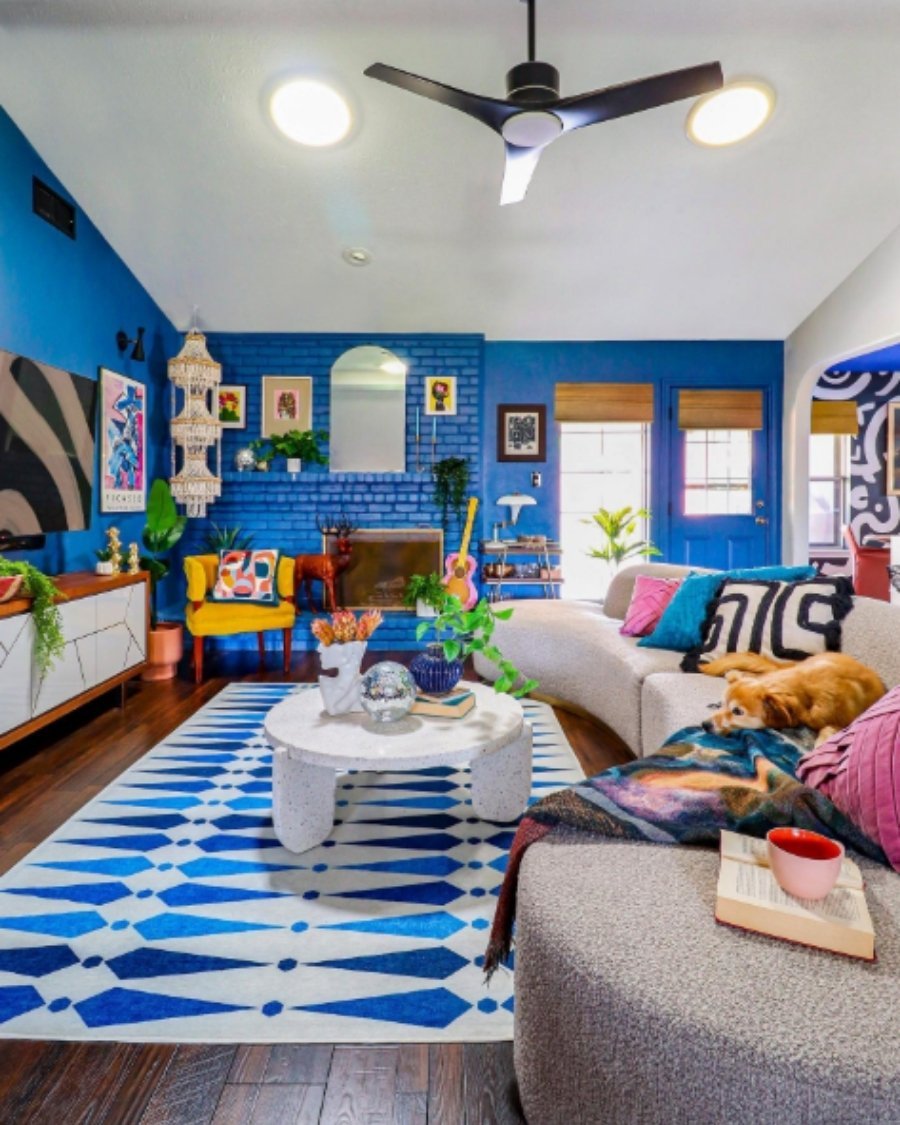 Eclectic living room with blue accent wall, geometric rug, yellow chair, and vibrant modern art.