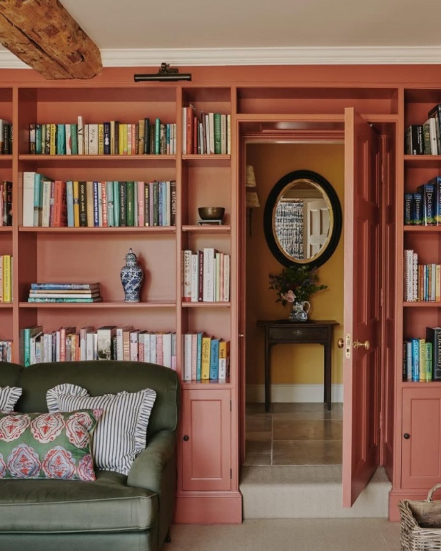 Eclectic library nook with terracotta bookshelves, green velvet sofa, and patterned pillows.