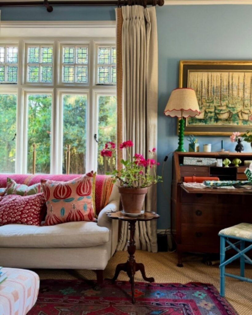 English cottage home with soft blue walls, floral curtains, vintage desk, and cozy pillows.