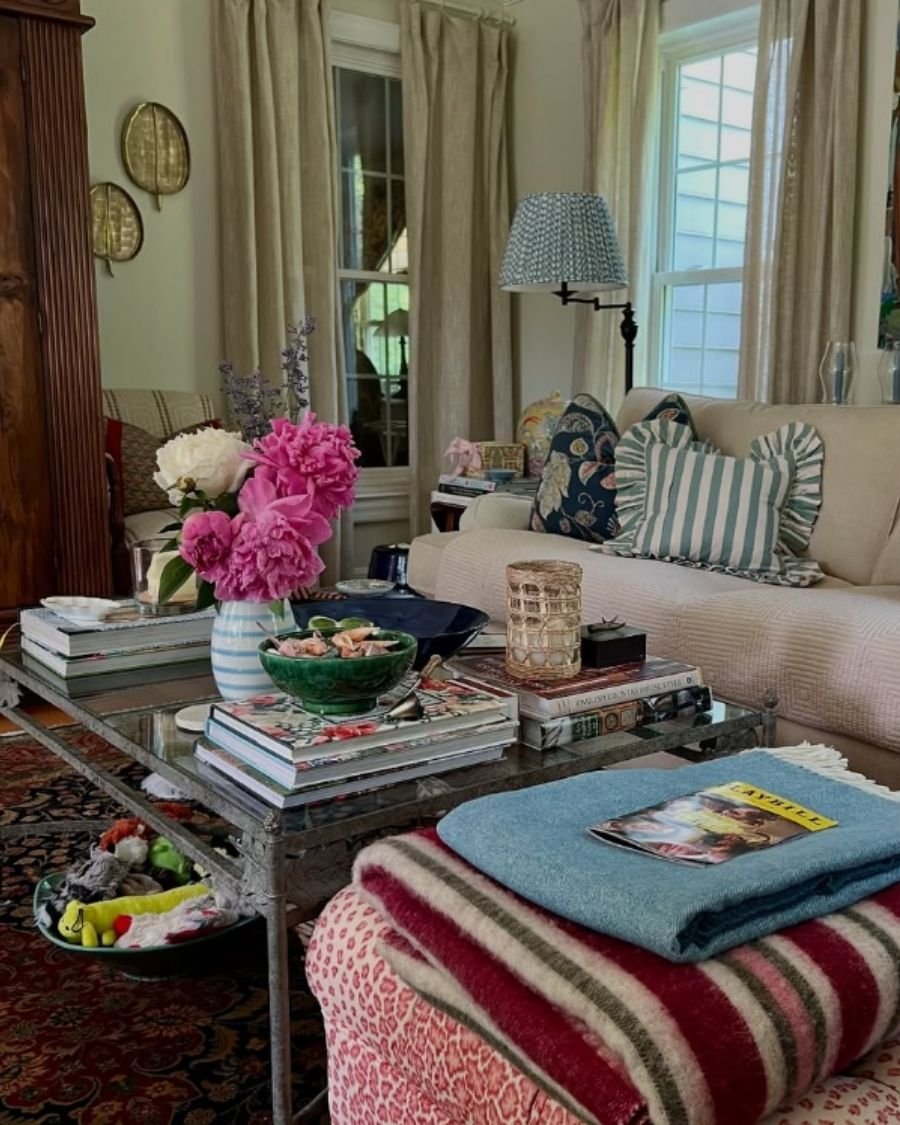 Eclectic living room with neutral sofa, patterned pillows, glass coffee table, and oriental rug.