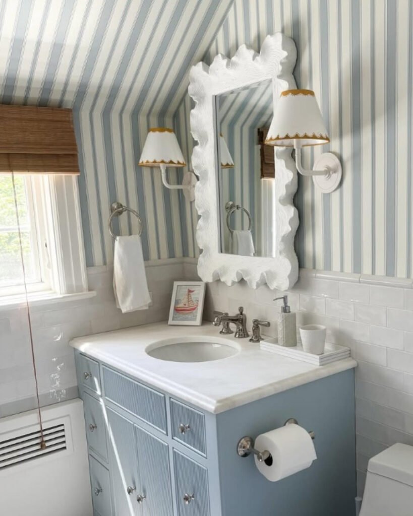 coastal style striped wallpaper bathroom with scalloped mirror and blue cabinet