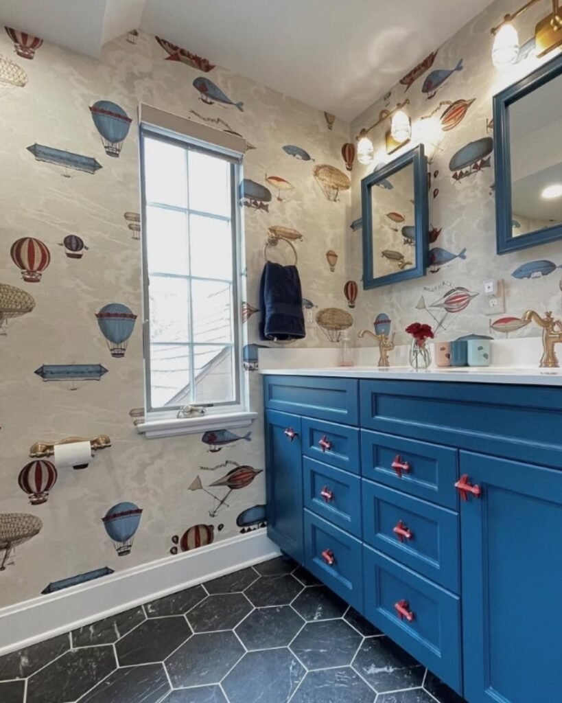 whimsical hot‑air‑balloon wallpaper bathroom with blue vanity and black hex‑tile floor