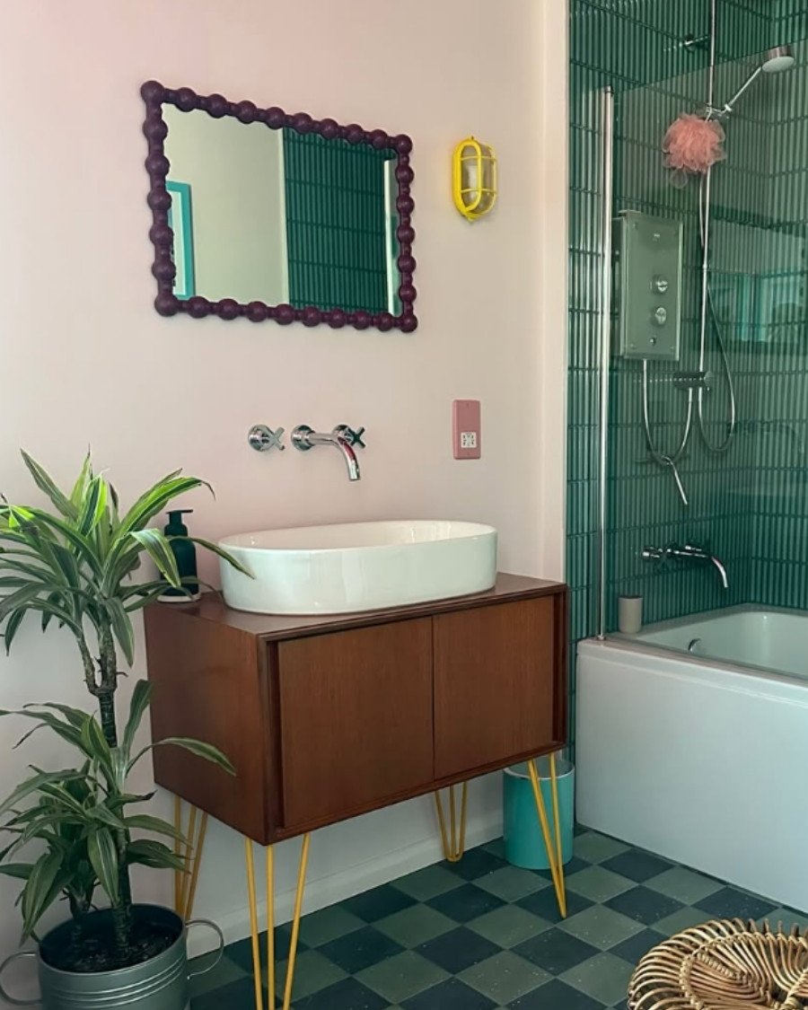 mid‑century style bathroom with green vanity, checkered floor, bubble mirror