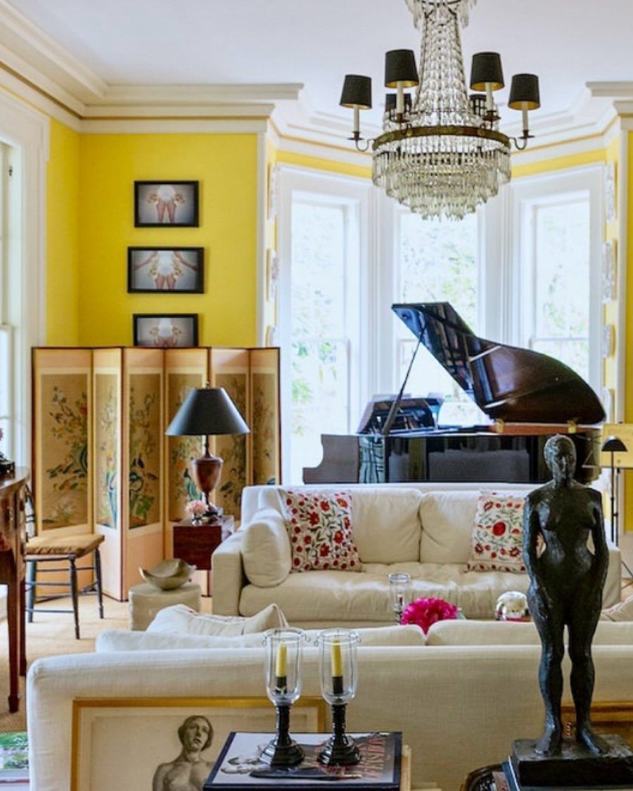 Eclectic living room with bright yellow walls, grand piano, crystal chandelier, and rich wood furniture.