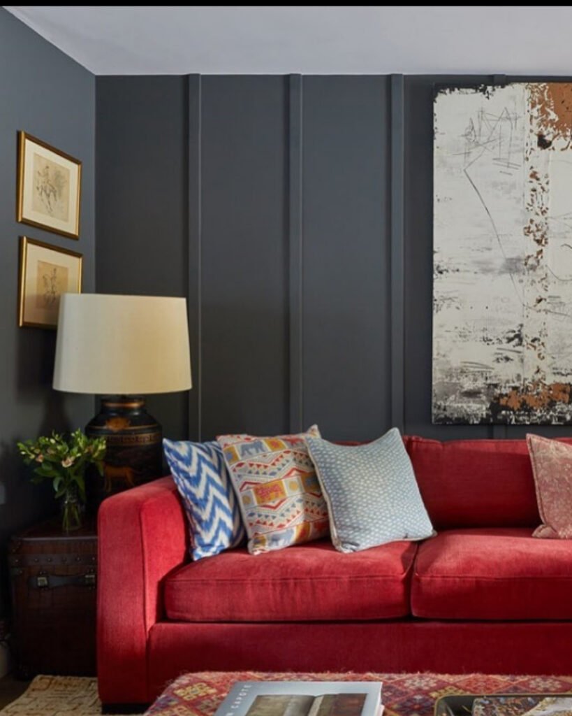 Vibrant red sofa with colorful cushions placed against a dark paneled wall, showcasing a bold unique sofa color