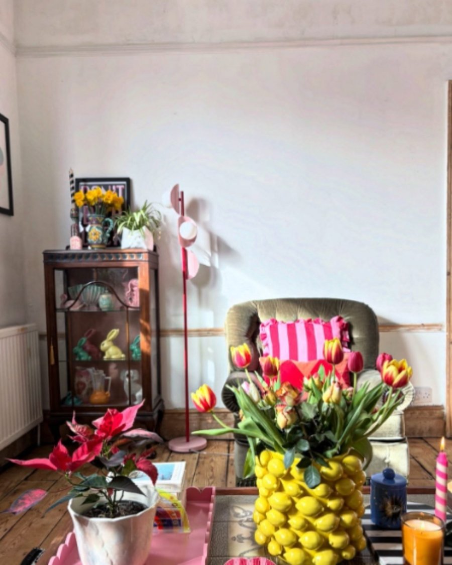 Eclectic living room corner with yellow pineapple vase, pink striped pillow, green armchair, and flowers.