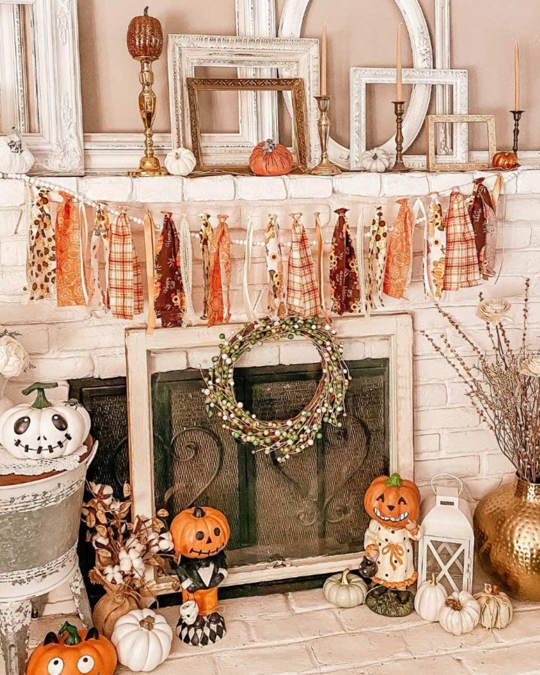 Soft and neutral fall mantel decor ideas with cream pumpkins, tassel garland, and layered vintage mirrors on a white brick fireplace.