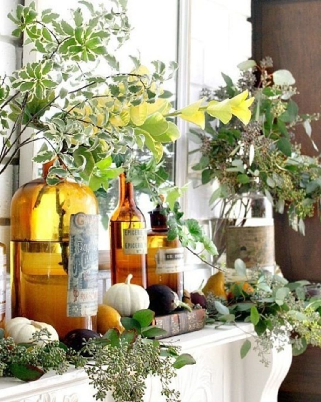  Natural fall mantel decorating ideas with amber bottles, green branches, and a few neutral pumpkins.