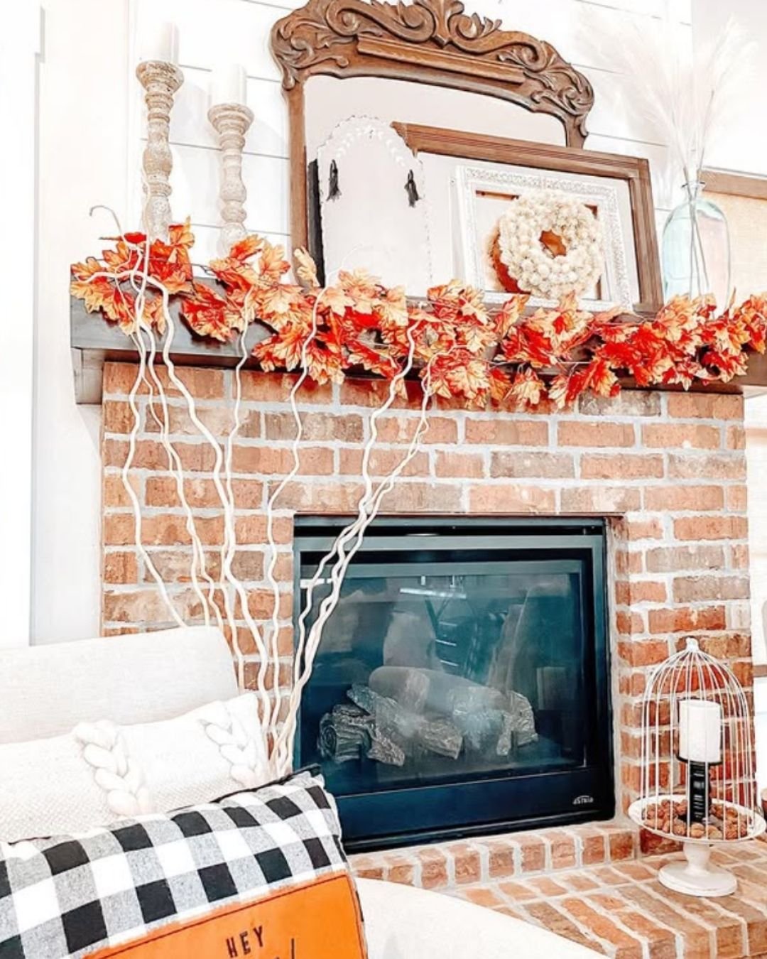 Cozy fall mantel decorating ideas with bright orange leaf garland, rustic mirror, white pumpkins, and lanterns on a brick fireplace.