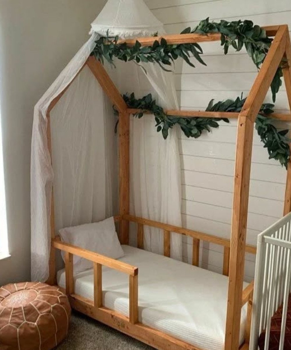 Simple Montessori bedroom with wood house-frame bed and leaf garland