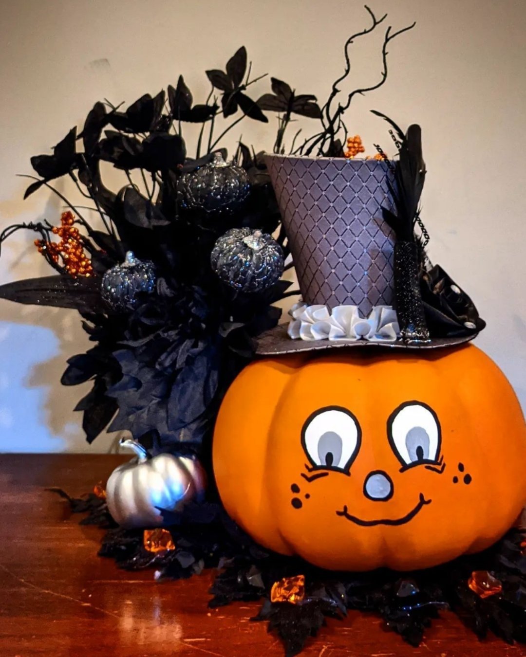 Pumpkin Decorating Ideas with hand-painted cartoon face, wearing a top hat, styled with black leaves and silver ornaments.
