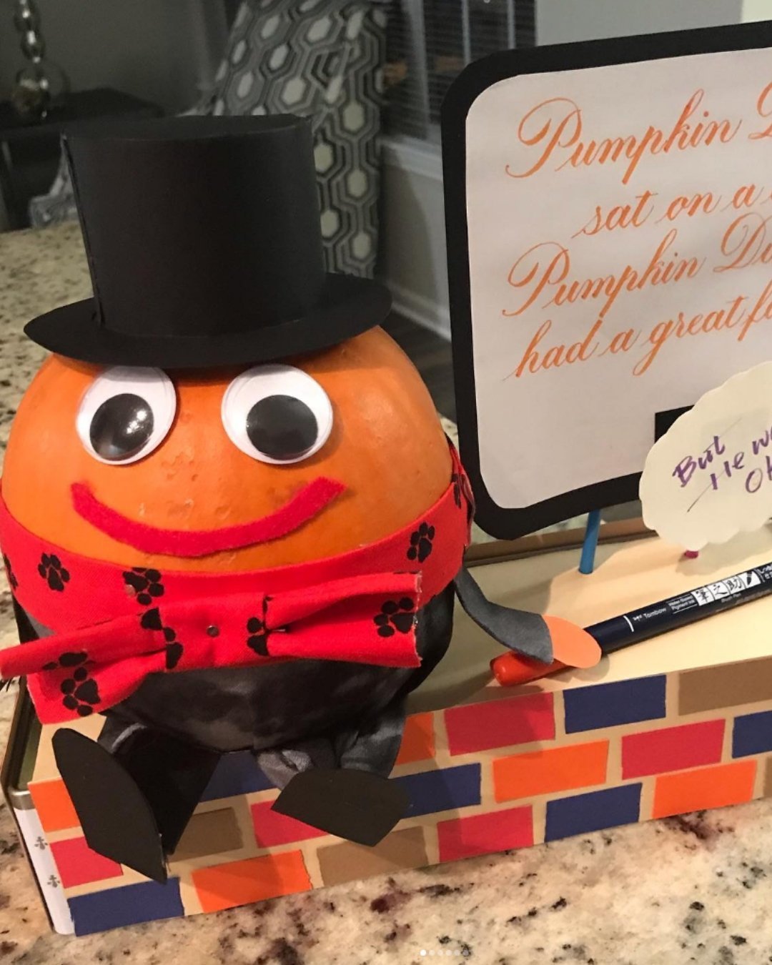 Cute Humpty Dumpty pumpkin decor with a top hat, bow tie, and googly eyes placed on a brick-themed box.