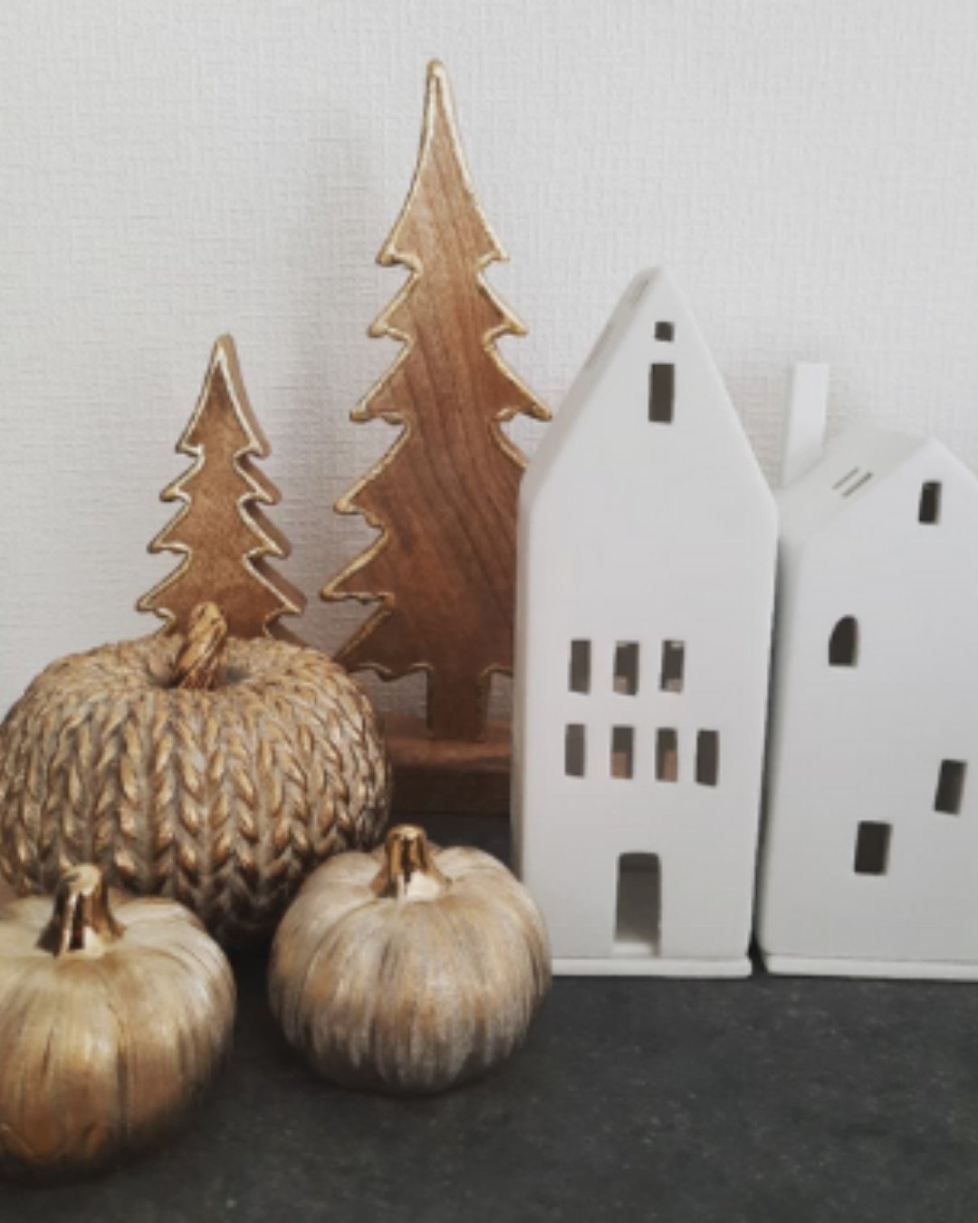 Golden textured pumpkins styled with white ceramic houses and wooden Christmas trees for a cozy Scandinavian-inspired fall decor.