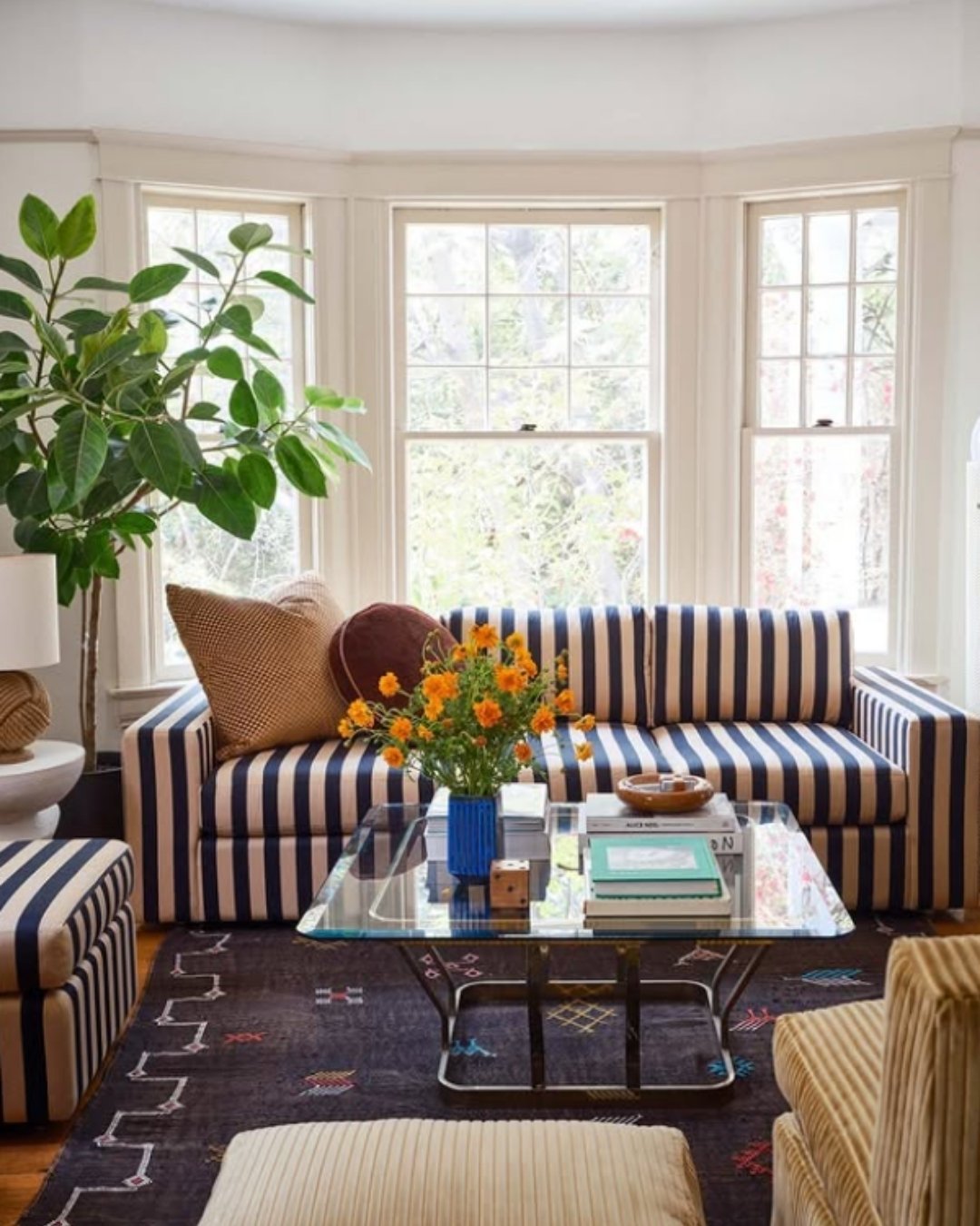 Navy striped sofa in a window bay area with bold rug and fresh flowers