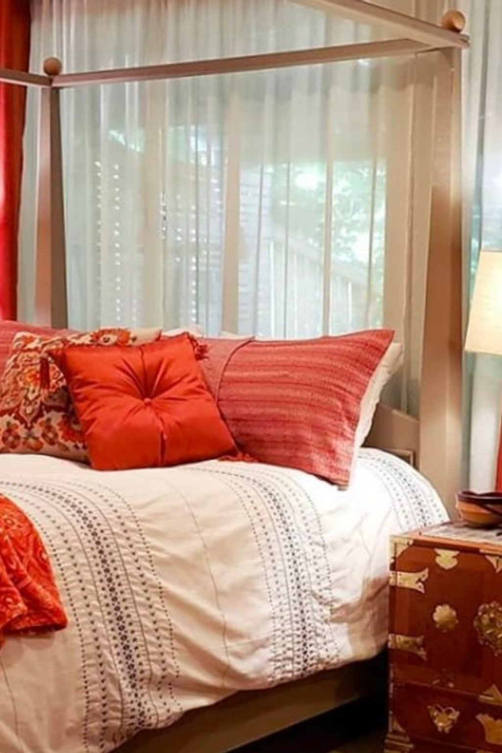 Canopy bed with white bedding and warm orange throw pillows—a cozy take on orange color bedroom ideas.