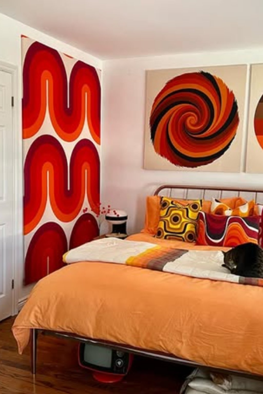 Groovy retro bedroom with orange swirl wall art, bold pillows, and solid orange bedding—funky orange color bedroom ideas for a playful space.