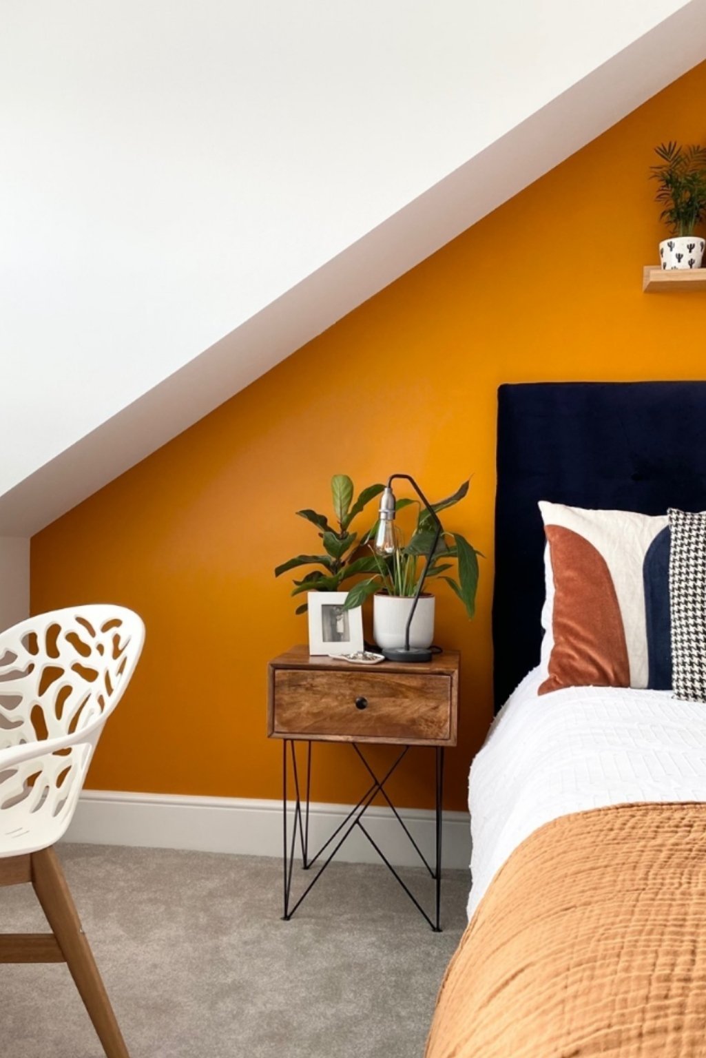 Sloped ceiling bedroom with mustard-orange feature wall and layered bedding—modern and minimal orange color bedroom ideas.