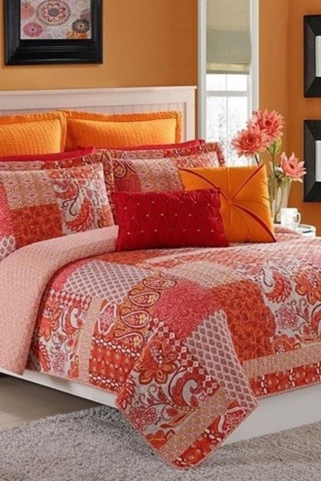 Vibrant bedroom with patchwork quilt, orange pillows, and soft-toned walls—a colorful take on orange color bedroom ideas.
