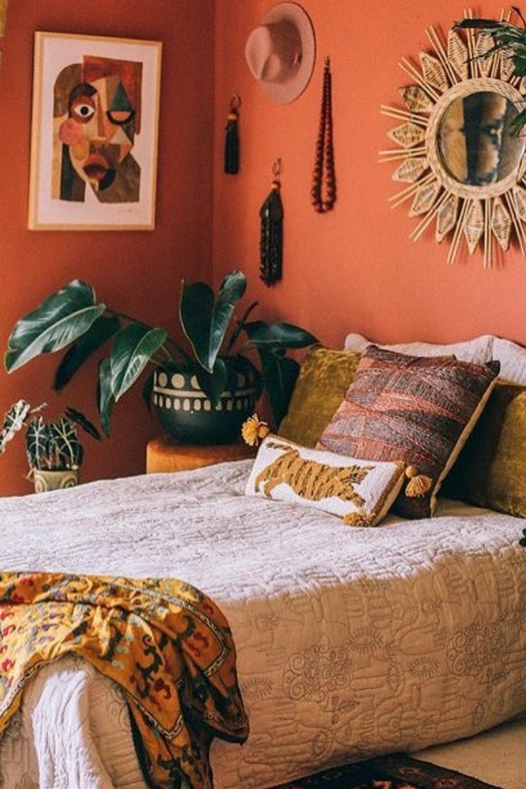 Boho-style bedroom with orange accent wall, tribal art, and earthy cushions showcasing unique orange color bedroom ideas.