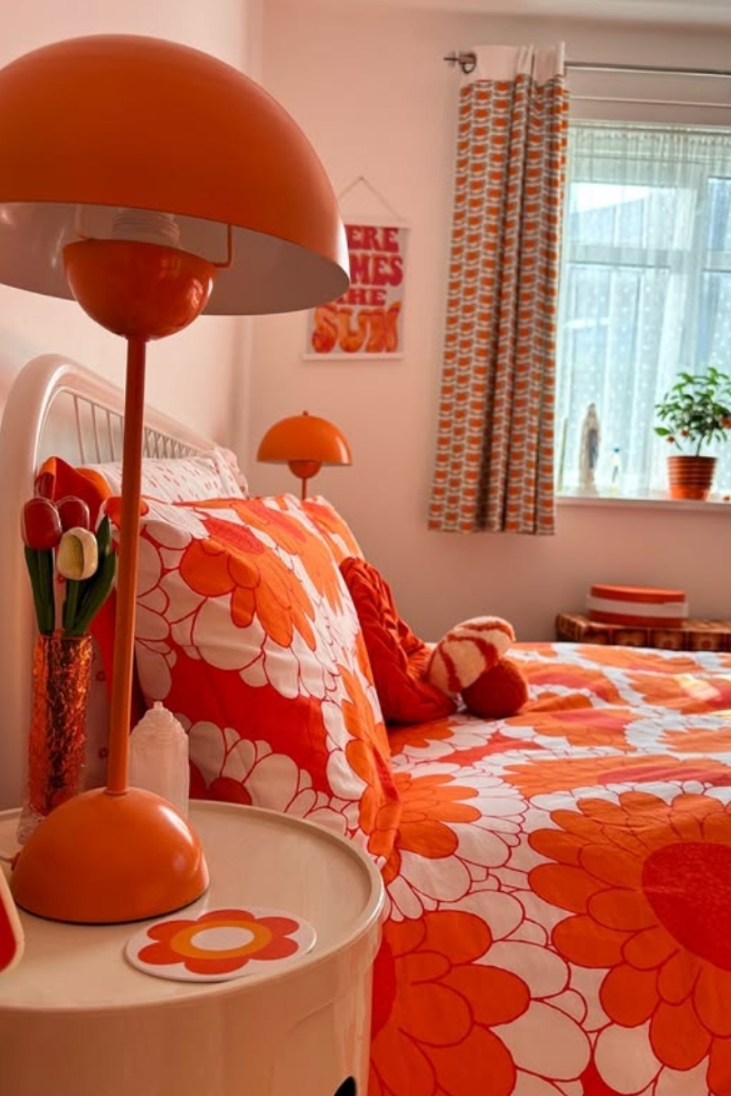Retro-inspired orange floral bedding with matching orange lamps and curtain—perfect for bold orange color bedroom ideas.