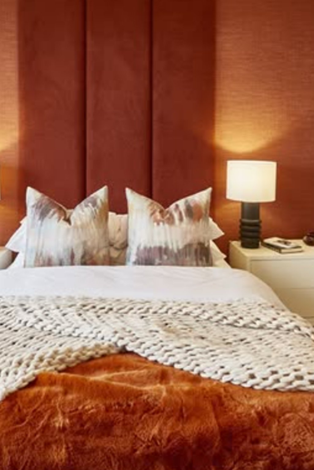 Elegant modern bedroom with burnt orange headboard, white bedding, and soft lighting.
