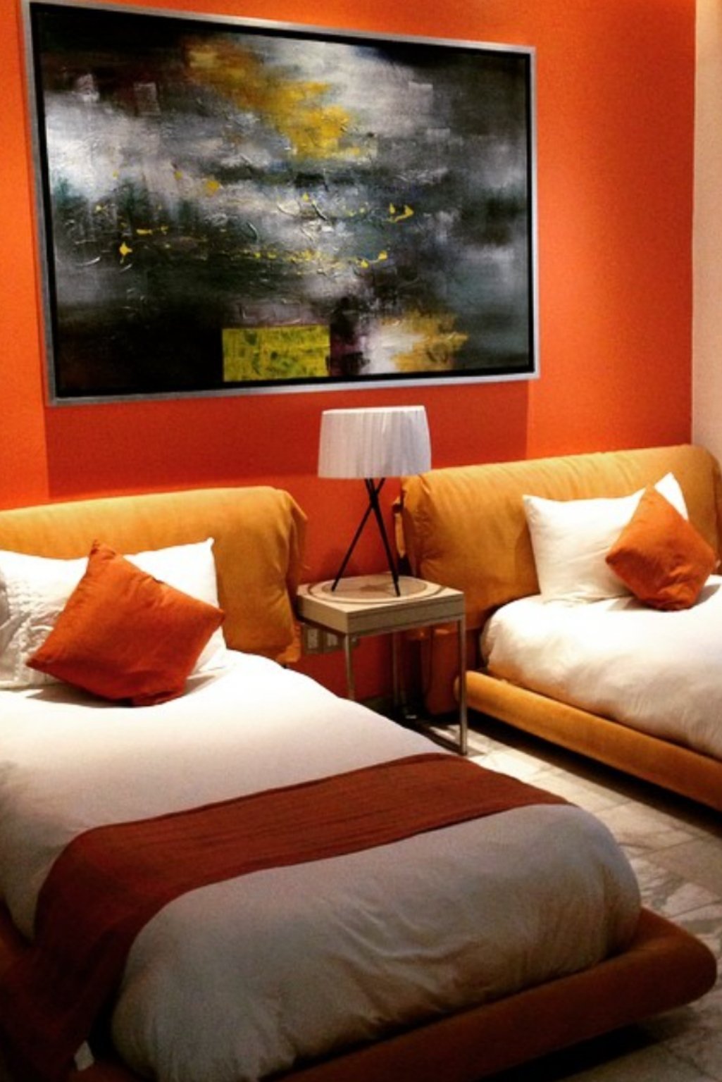 Orange accent wall behind twin beds with matching throw pillows and moody abstract art.