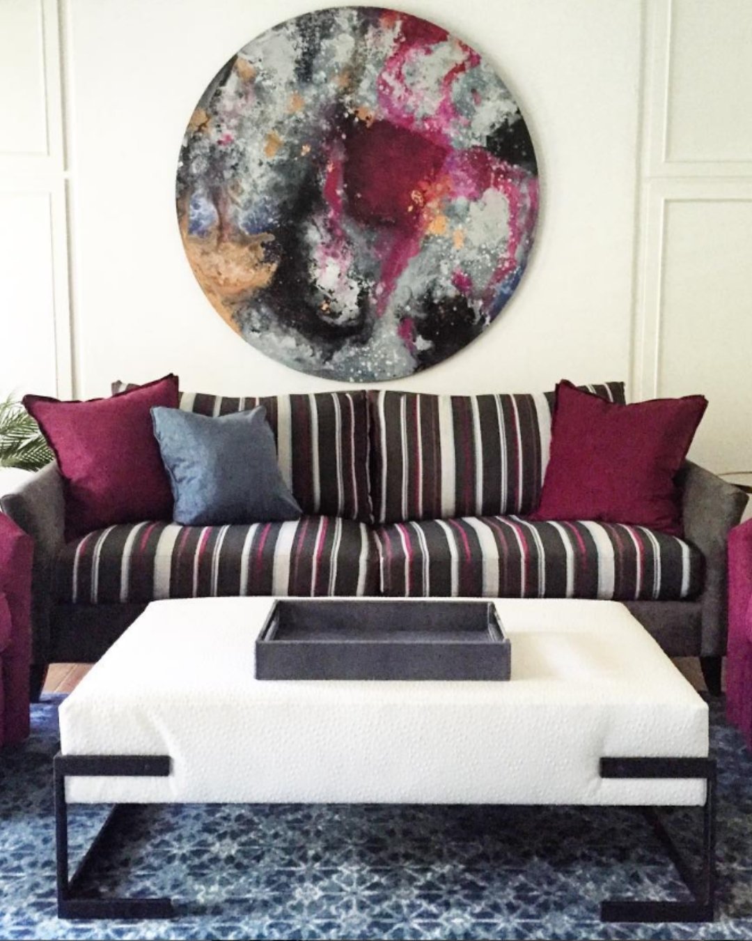 Plum striped sofa with round abstract art and blue area rug.