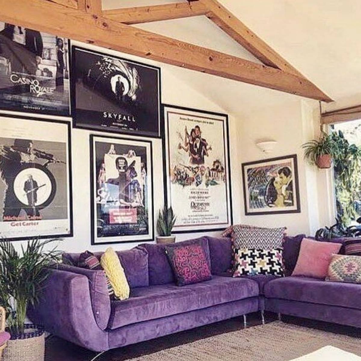 Purple sectional sofa with graphic wall art and wooden ceiling beams in a bright, cozy living room.
