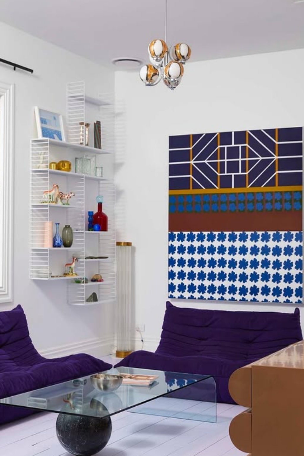 Modern room with mid-century purple sofa and geometric wall art on white walls.