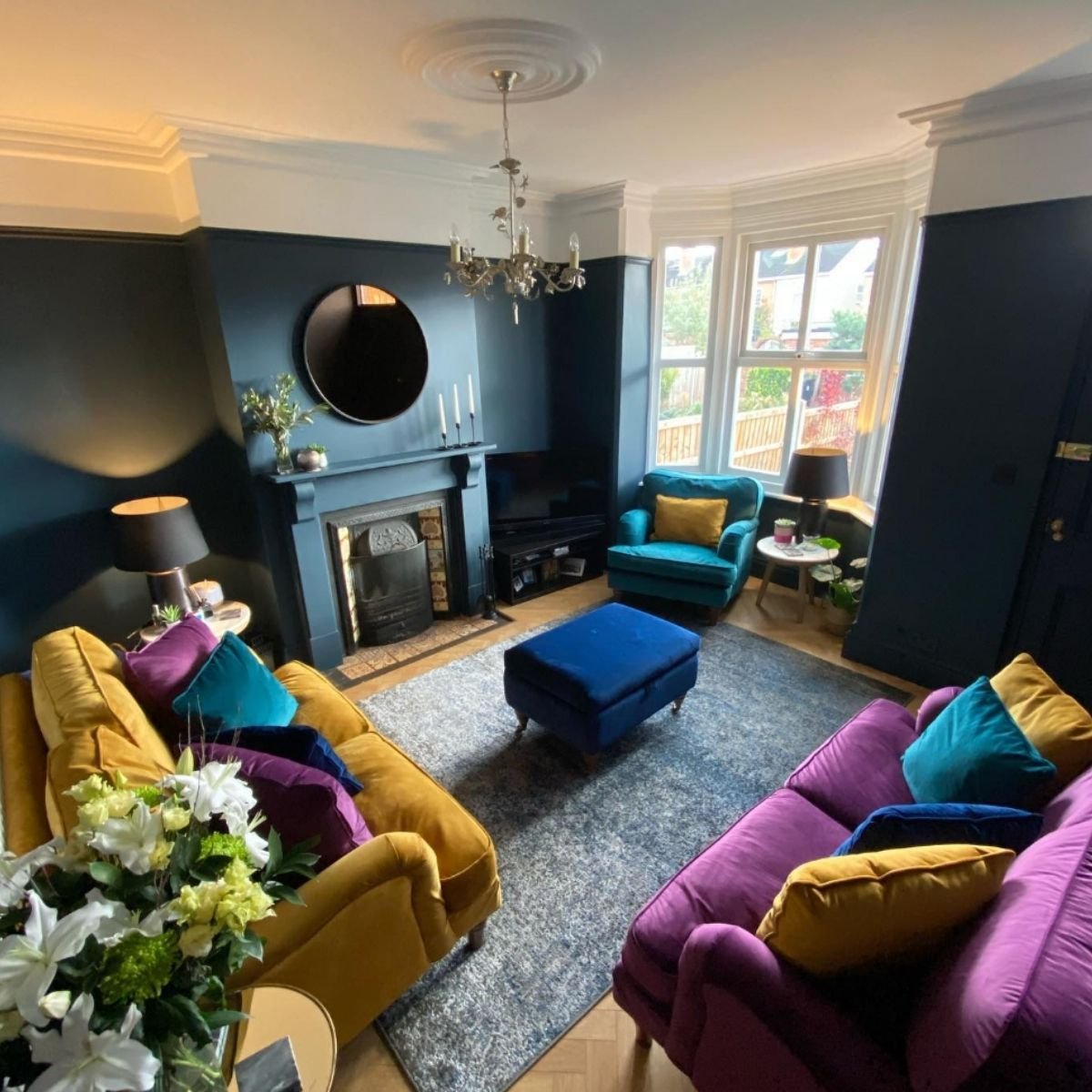 Colorful living space with purple sofas, mustard cushions, and teal accents.