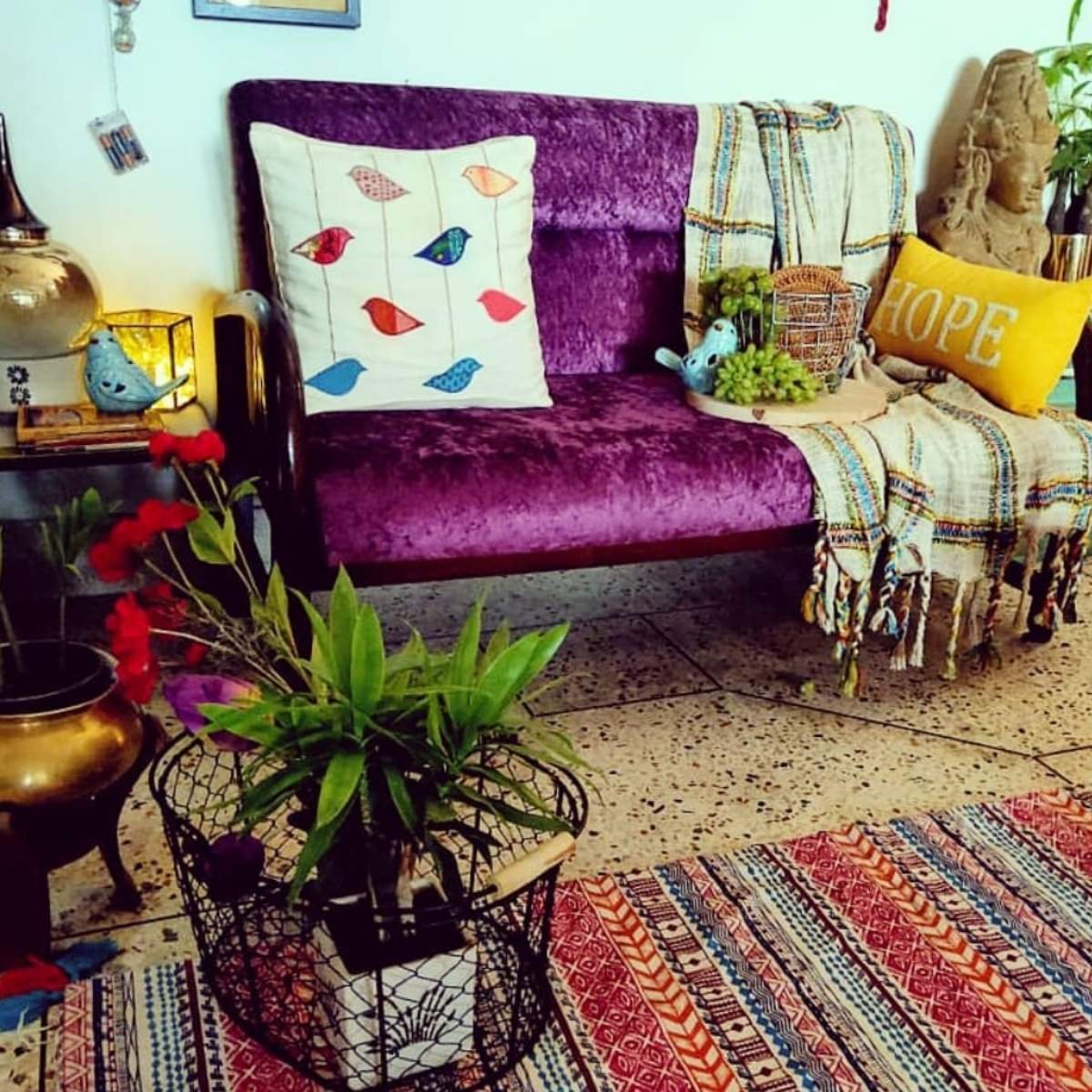 Crafty styled space with embroidered pillows, layered rugs, and a purple sofa.