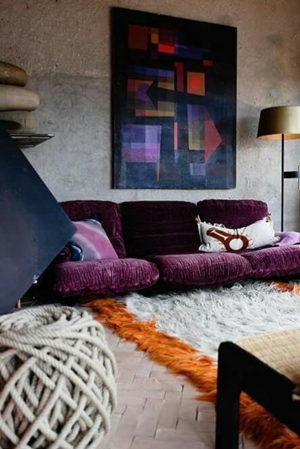 Industrial decor with purple velvet sofa, concrete wall, and graphic art.
