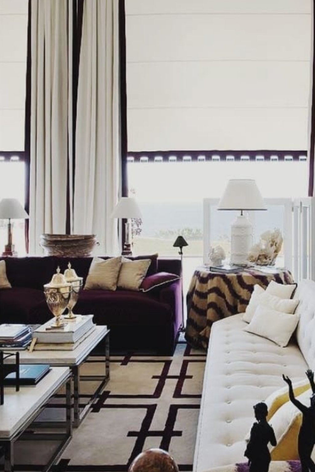 Plum purple sofa in a light-filled room with white curtains and soft flooring.