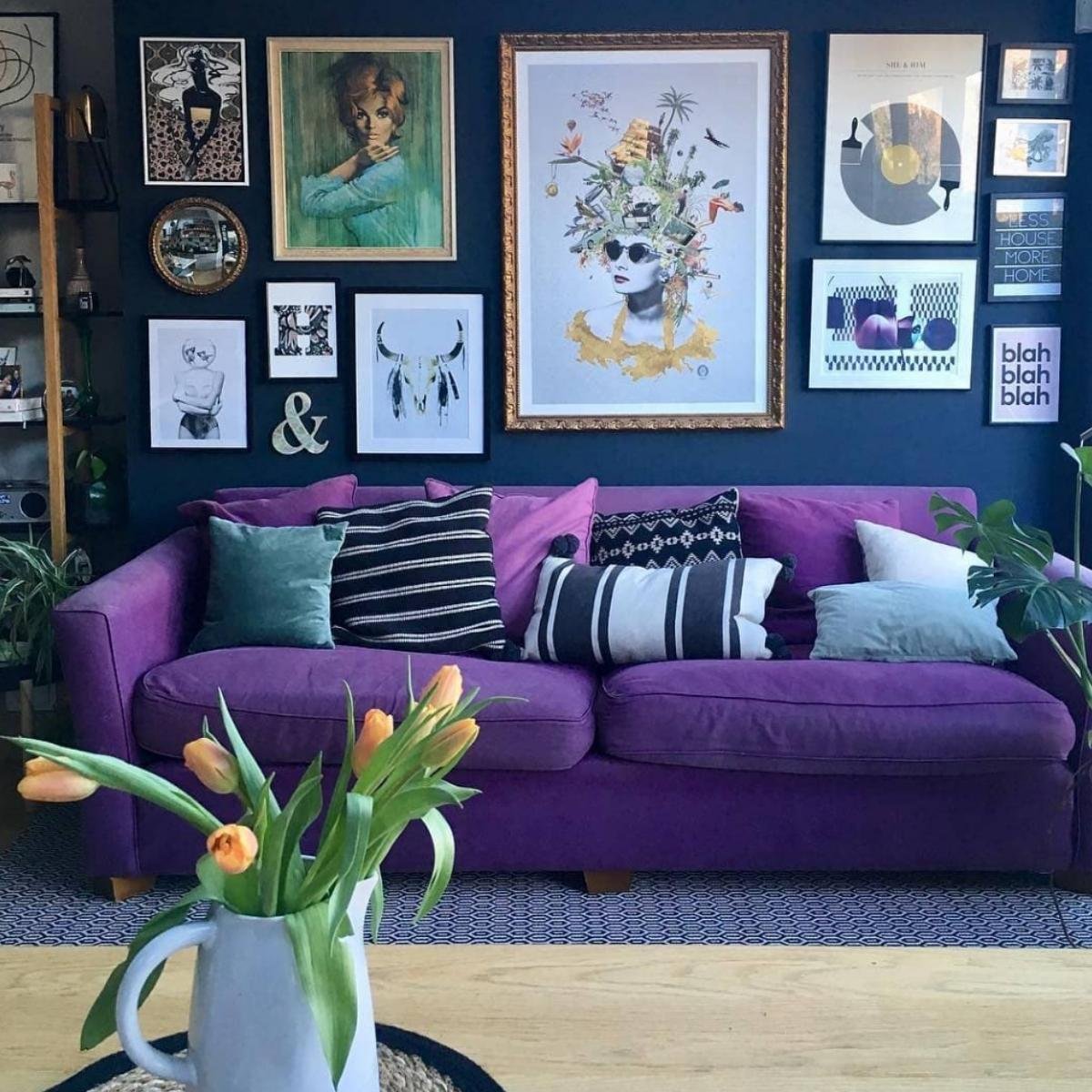 Deep purple sofa against a navy gallery wall with colorful pillows and fresh tulips on a table.