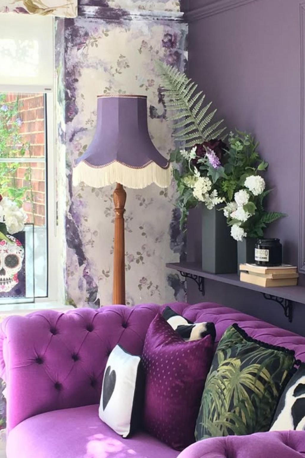 Soft lilac sofa with vintage floor lamp, leafy plant, and textured purple wall behind.