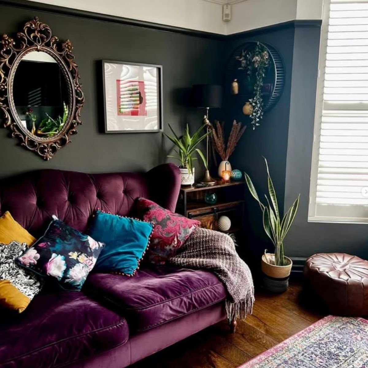 Plum velvet sofa in an eclectic room with a vintage mirror and dark walls.