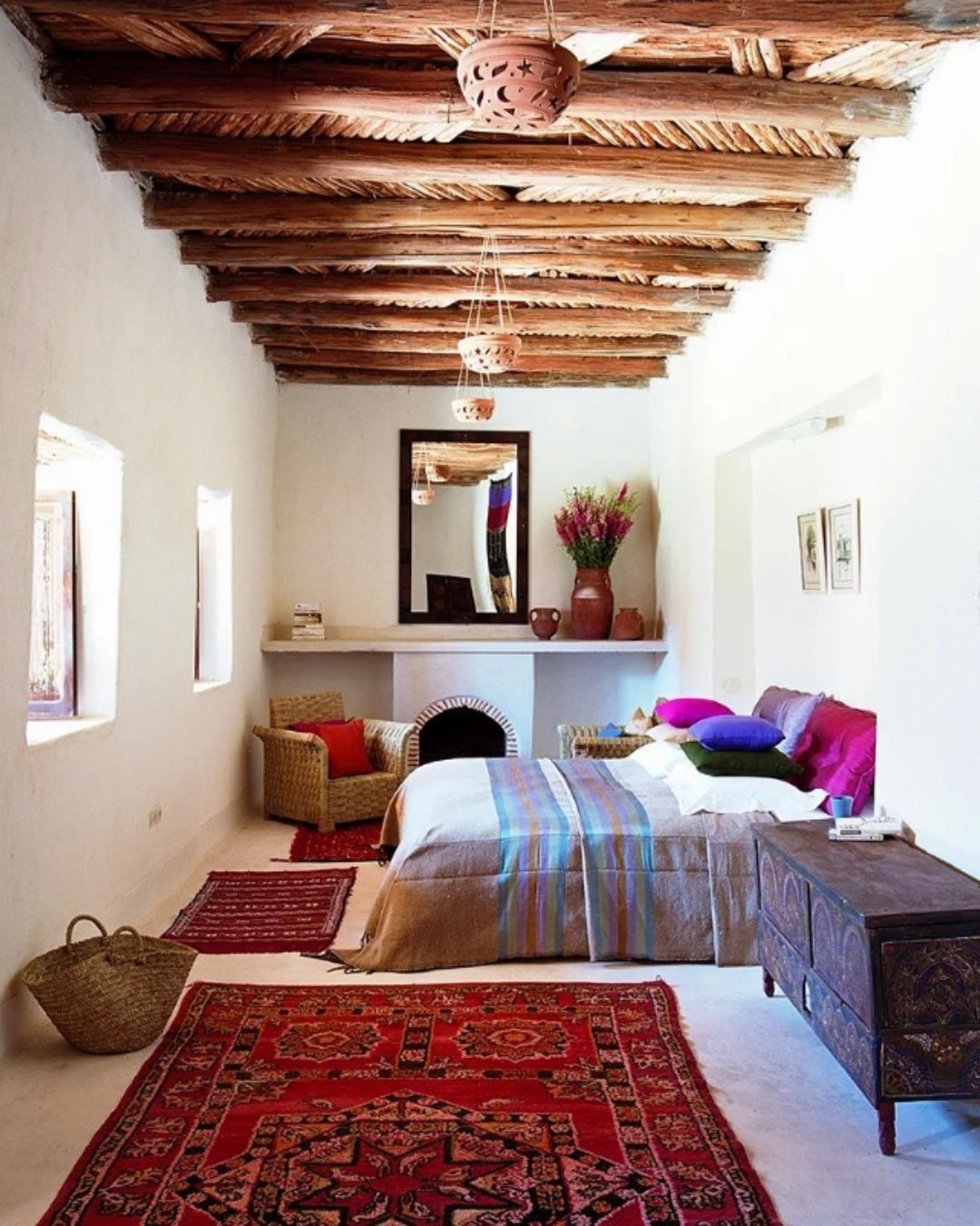 White bedroom with wooden ceiling beams, red rugs, and minimal decor