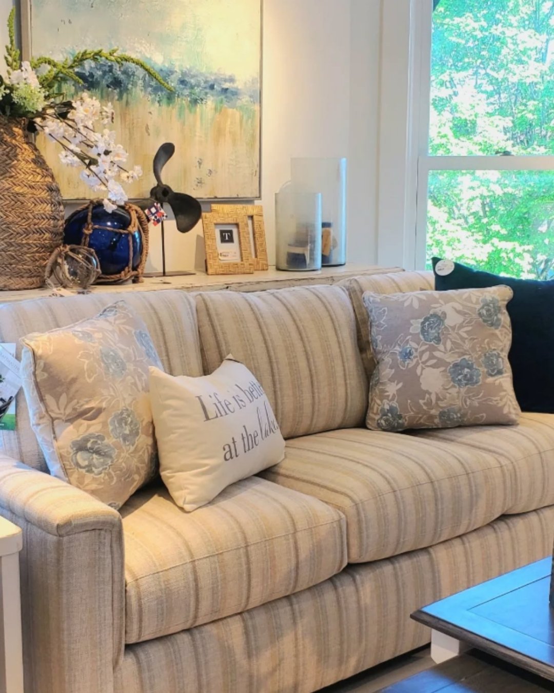 Soft neutral striped sofa with blue and beige floral pillows and coastal decor