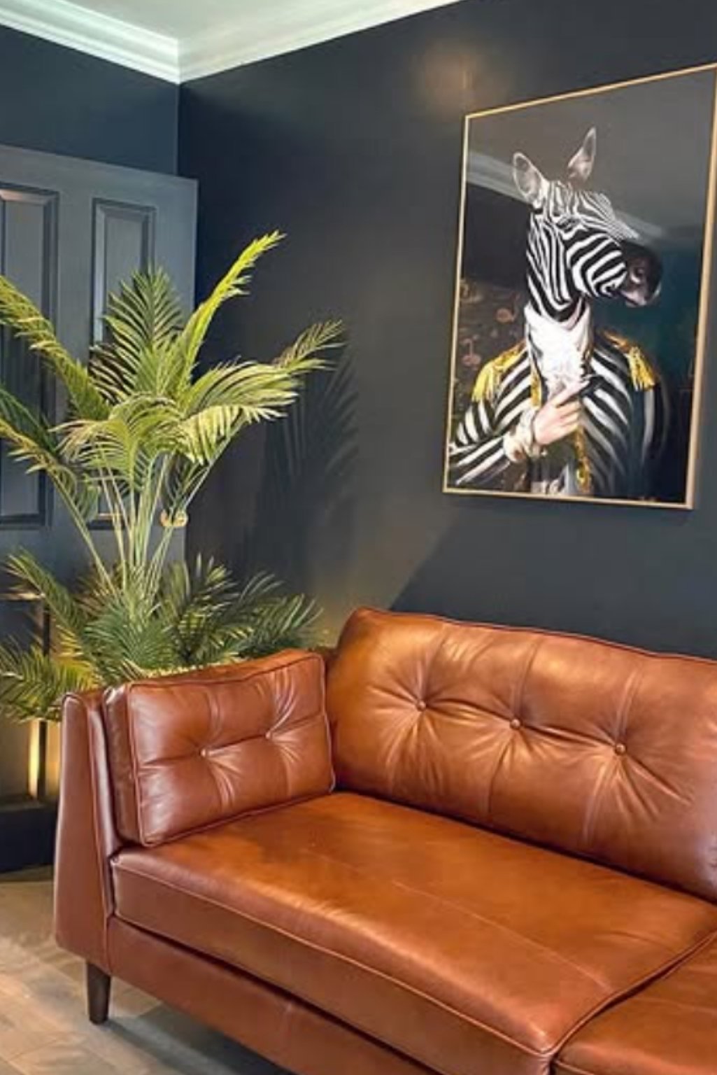 Moody living room with navy blue wall, tan leather sofa, and zebra art