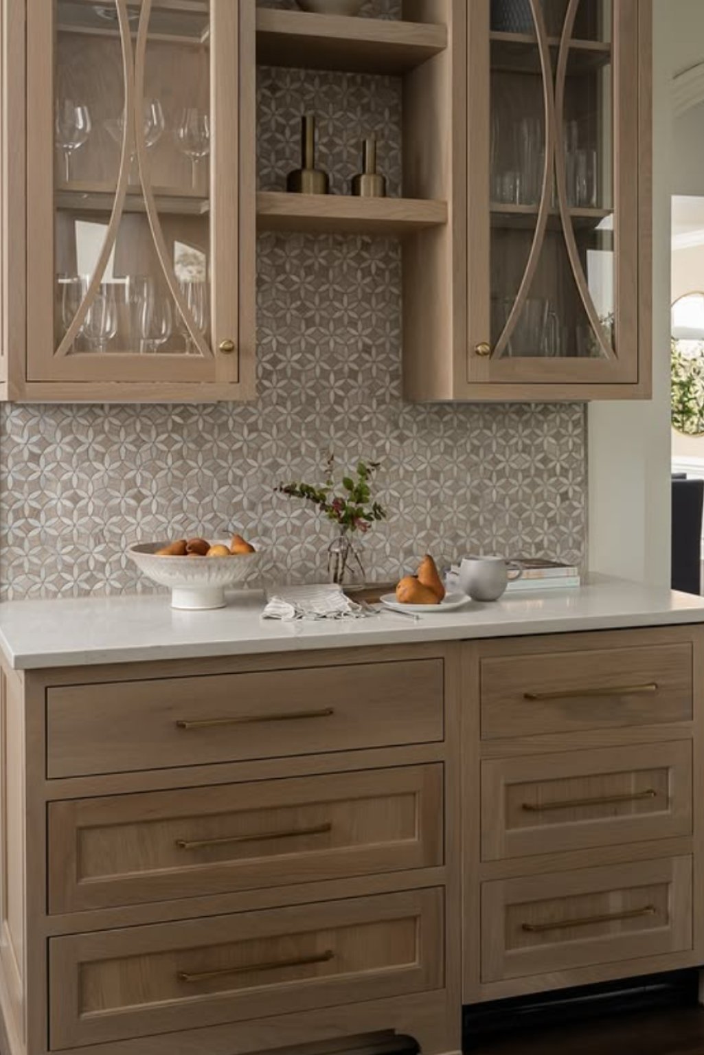Light-toned white oak kitchen cabinets styled with patterned tile backsplash and golden hardware, blending into a transitional design.