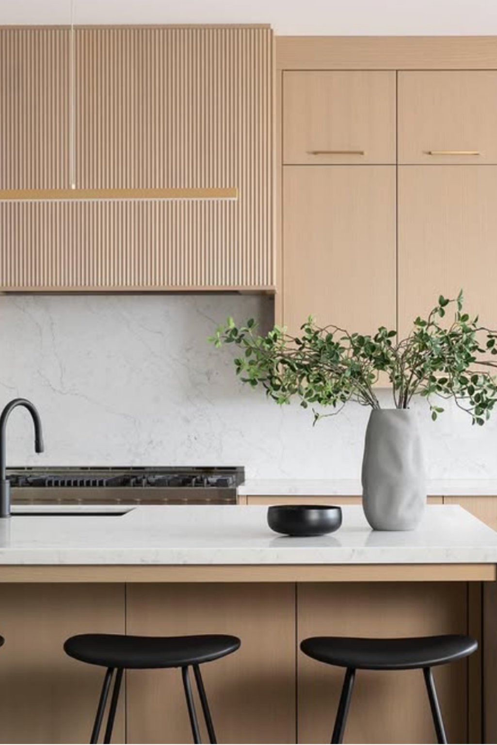 Modern kitchen with white oak kitchen cabinets featuring vertical slatted doors, paired with a white stone backsplash and minimalist decor.