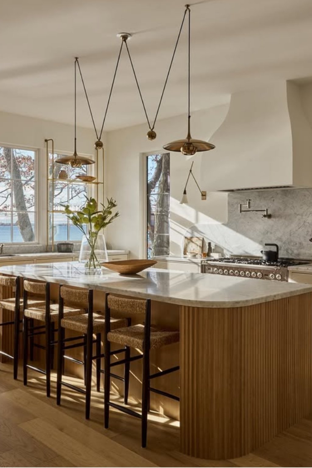 White oak kitchen cabinets featuring vertical slatted island design, paired with marble countertops and sculptural pendant lights in a sunlit kitchen.